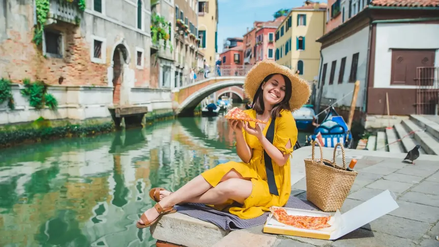 dívka si vychutnává pizzu na chodníku poblíž kanálu v Benátkách