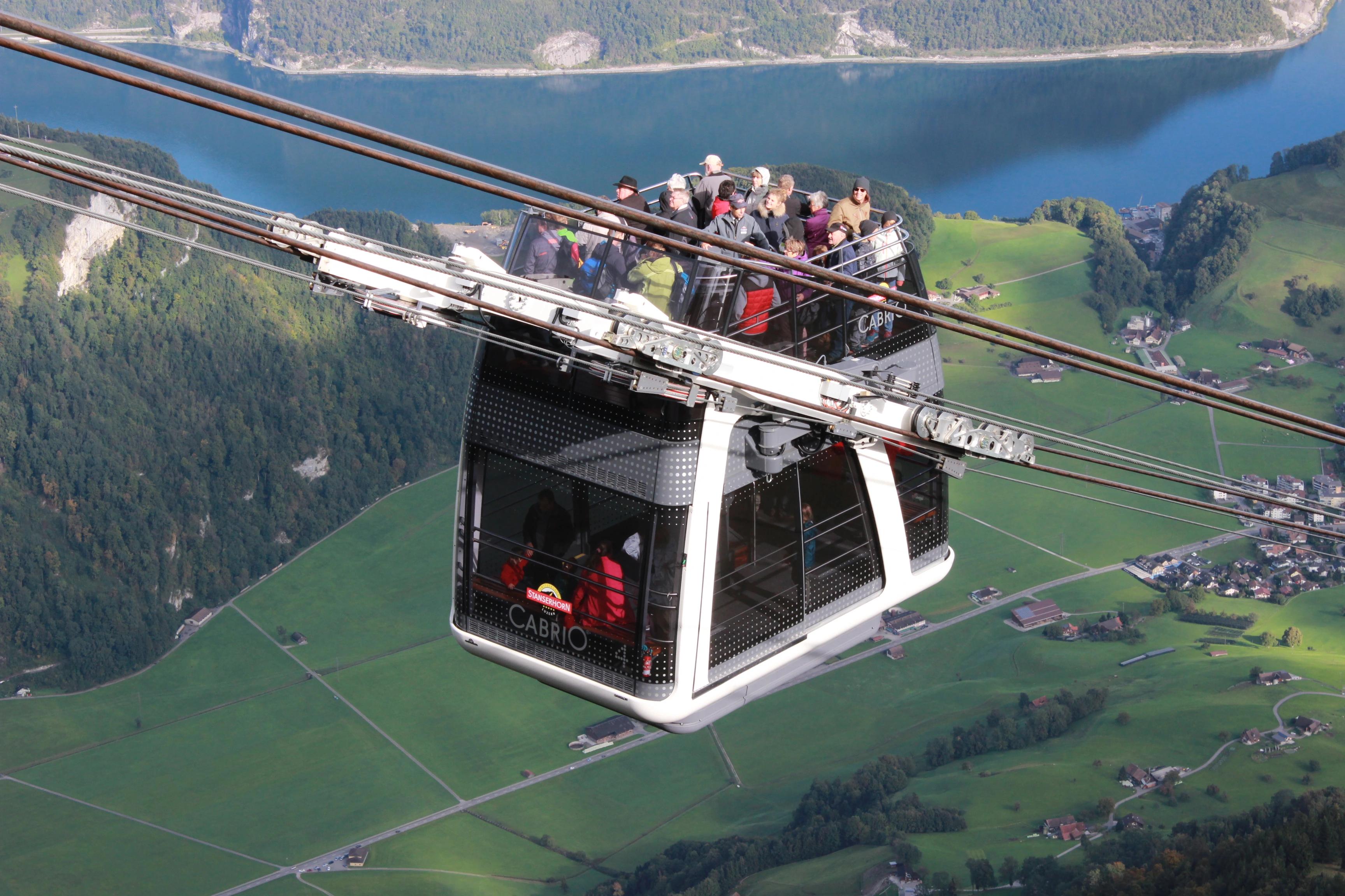 Skupina lidí jedoucí v dvoupatrové kabině lanovky Cabrio s otevřenou střechou v Stanserhorn, Švýcarsko