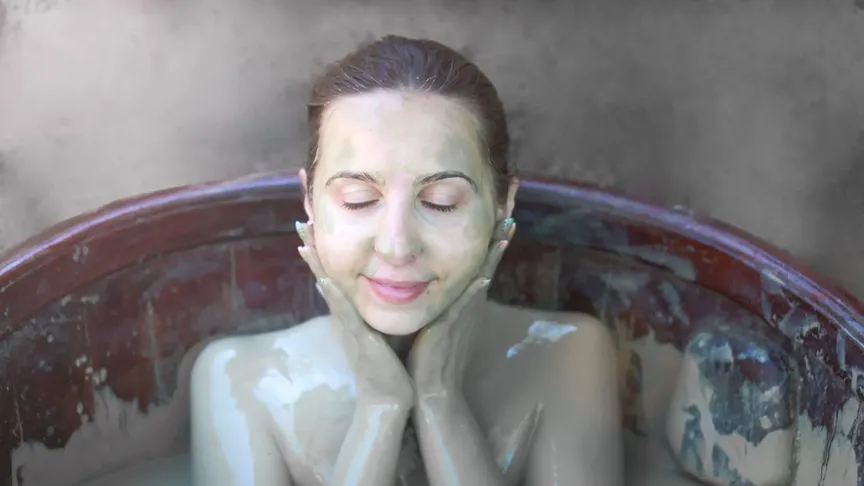Mladá žena se koupel v bahenní lázni. Je do ní ponořen a bahno si rozetírá po obličeji.