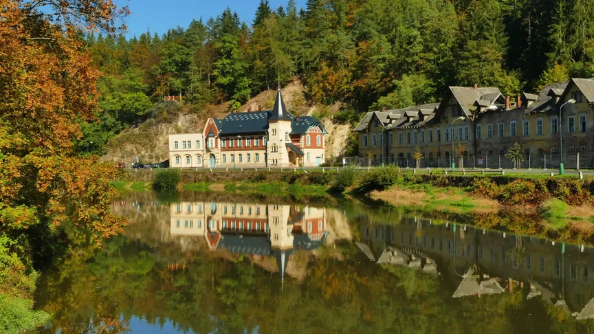 Pohled na lázně kyselka. V popředí chátrající budovy za kterými je vidět nově opravená stavba