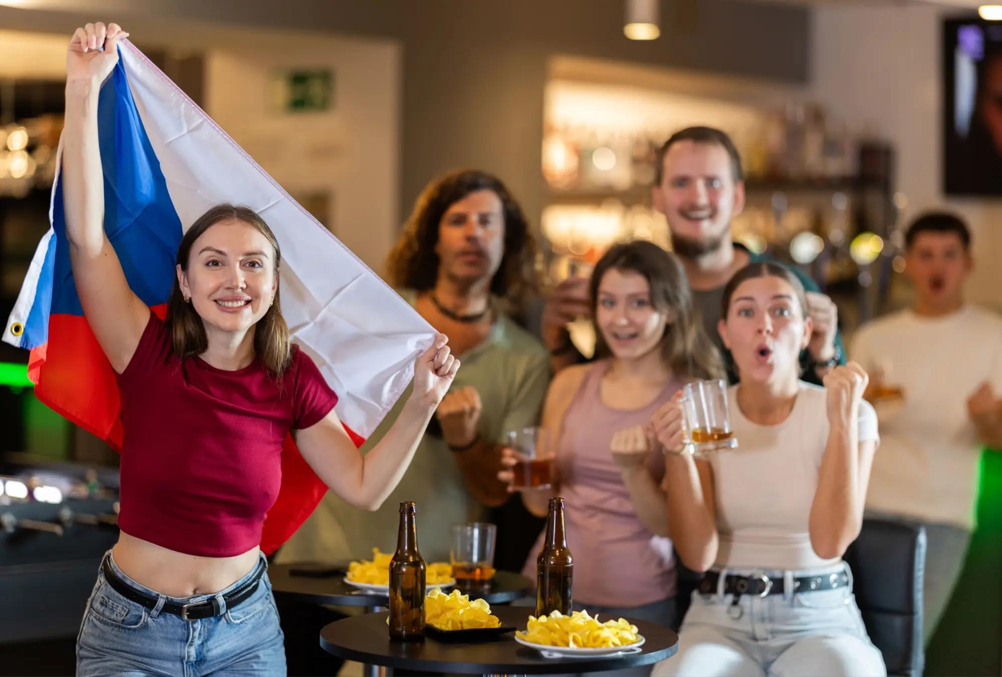 Čeští fanoušci s vlajkou fandí při sportovním utkání