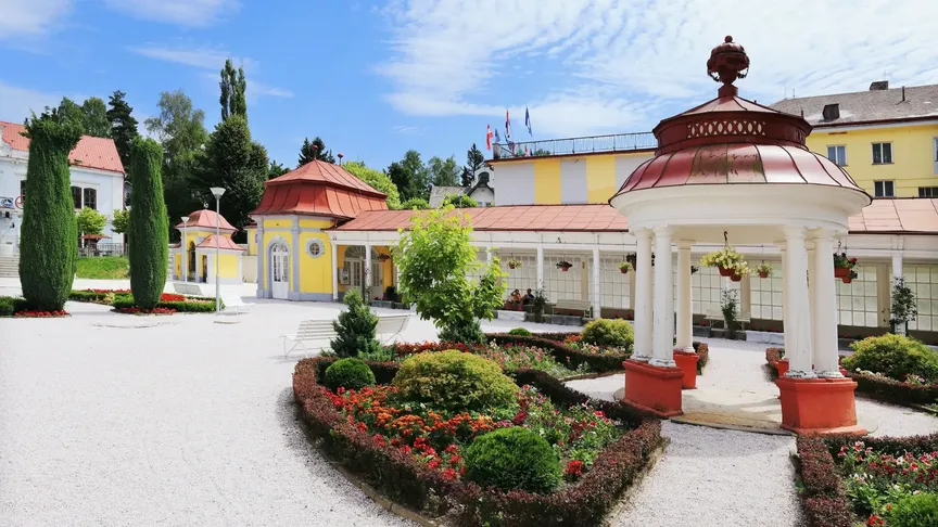 Na obrázku jsou lázně Libverda s krásnými pavilony a květinami. Je krásný den, na obloze je jen pár mraků, jinak je modrá.