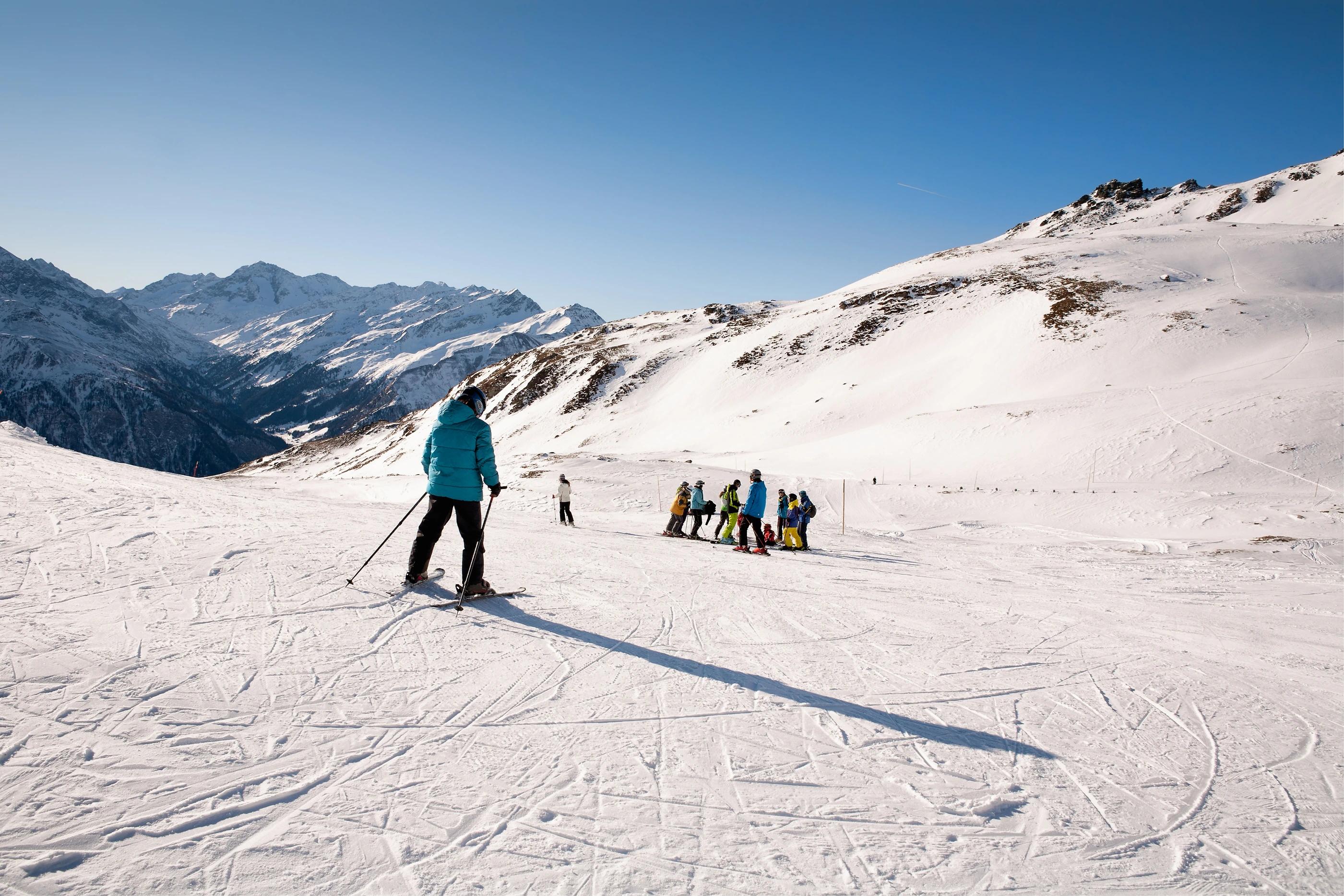 Lyžař na svazích Scharecku jede směrem ke skupině ostatních postávajících lyžařů