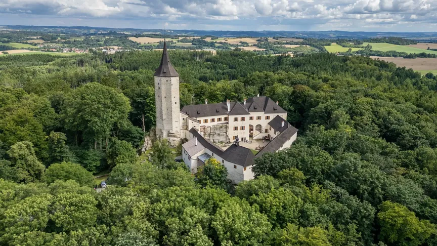Panoramatický záběr na hrad Roštejn s jeho hradbami a věží. Leží uprostřed lesa, takže jde vidět mnoho stromů.