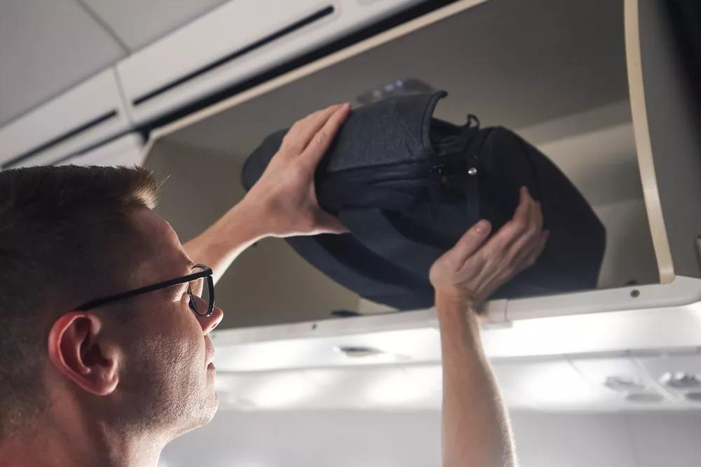 muž ukládající batoh do přihrádky nad sedadly v letadle