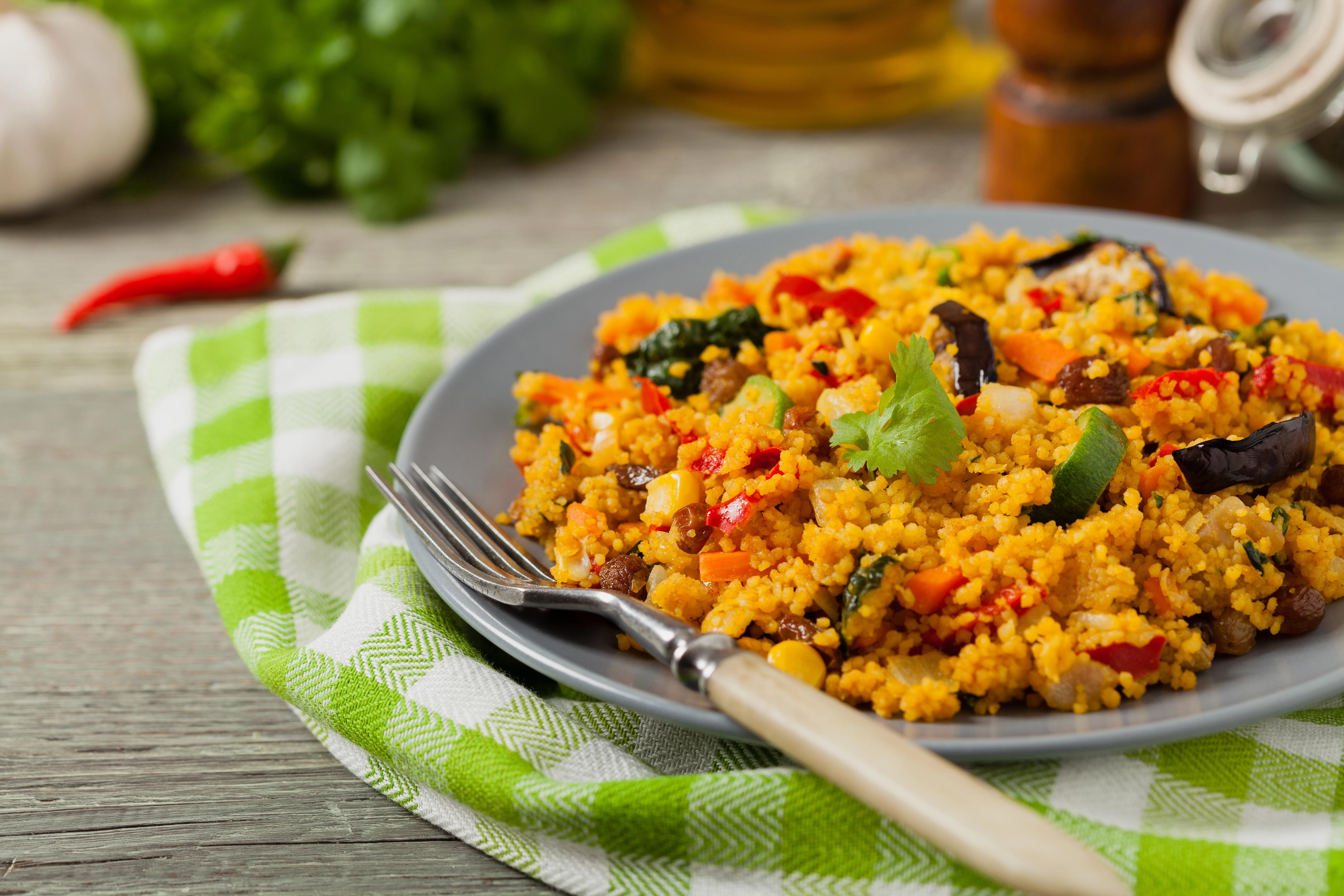 Na stole leží zeleno-bílé kostkované prostírání, na kterém se nachází šedý talíř s kuskusem, zeleninou a položenou vidličkou