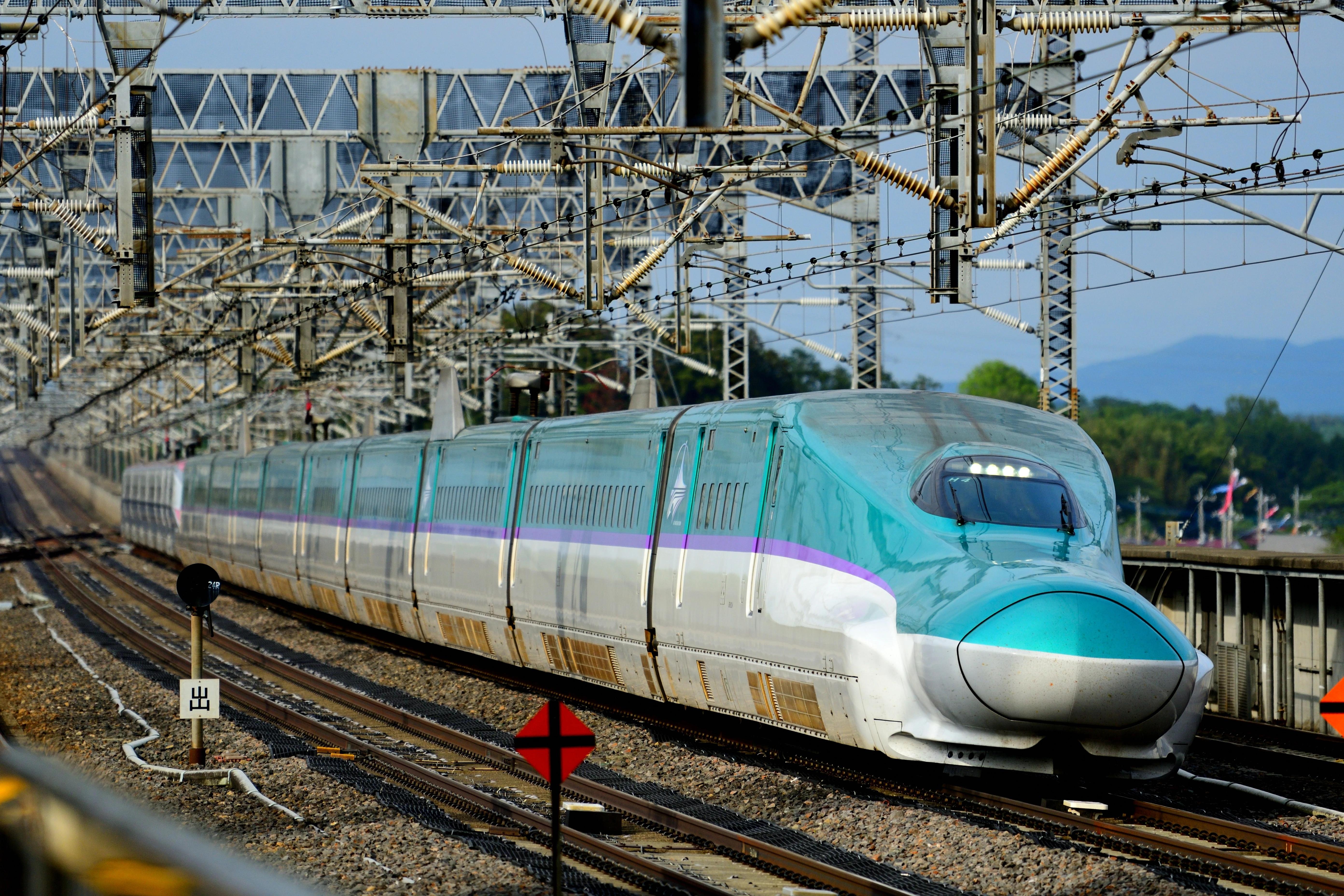 Azurovo-bílý vlak JR Hokkaido H5 Shinkansen projíždí stanicí Nasushiobara za slunečného počasí