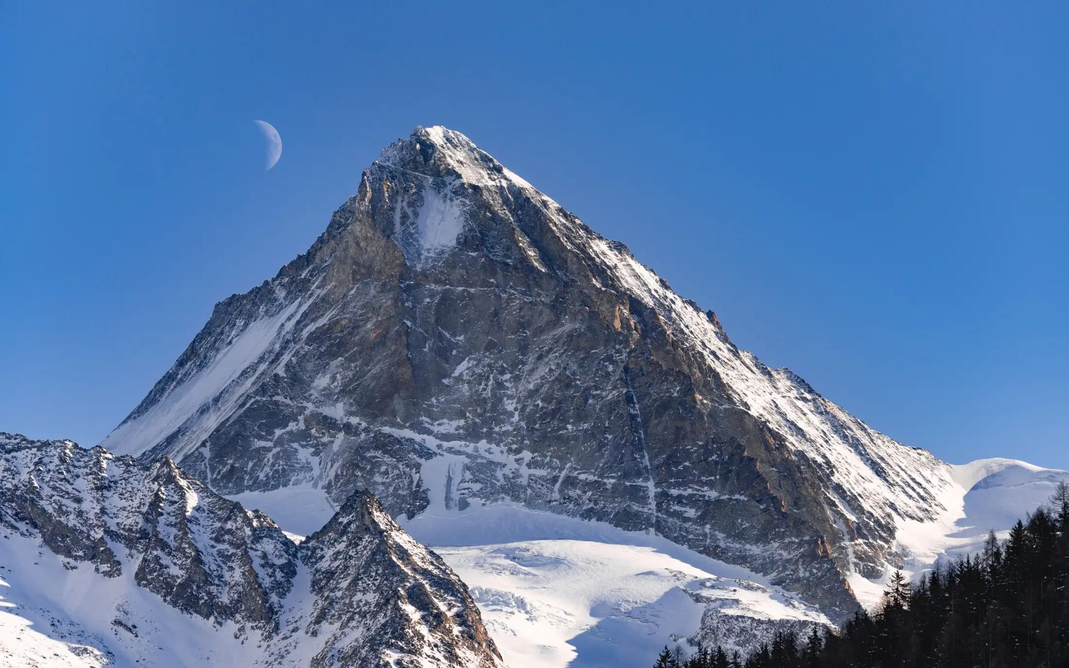 Záběr na Mount Everest za krásného slunečného dne. Na obloze není ani mráček. Hora je pokrytá sněhem a stejně tak její okolní vrcholky.