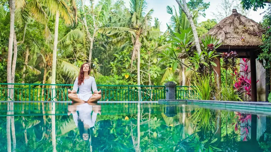 žena medituje u bazénu pod palmami