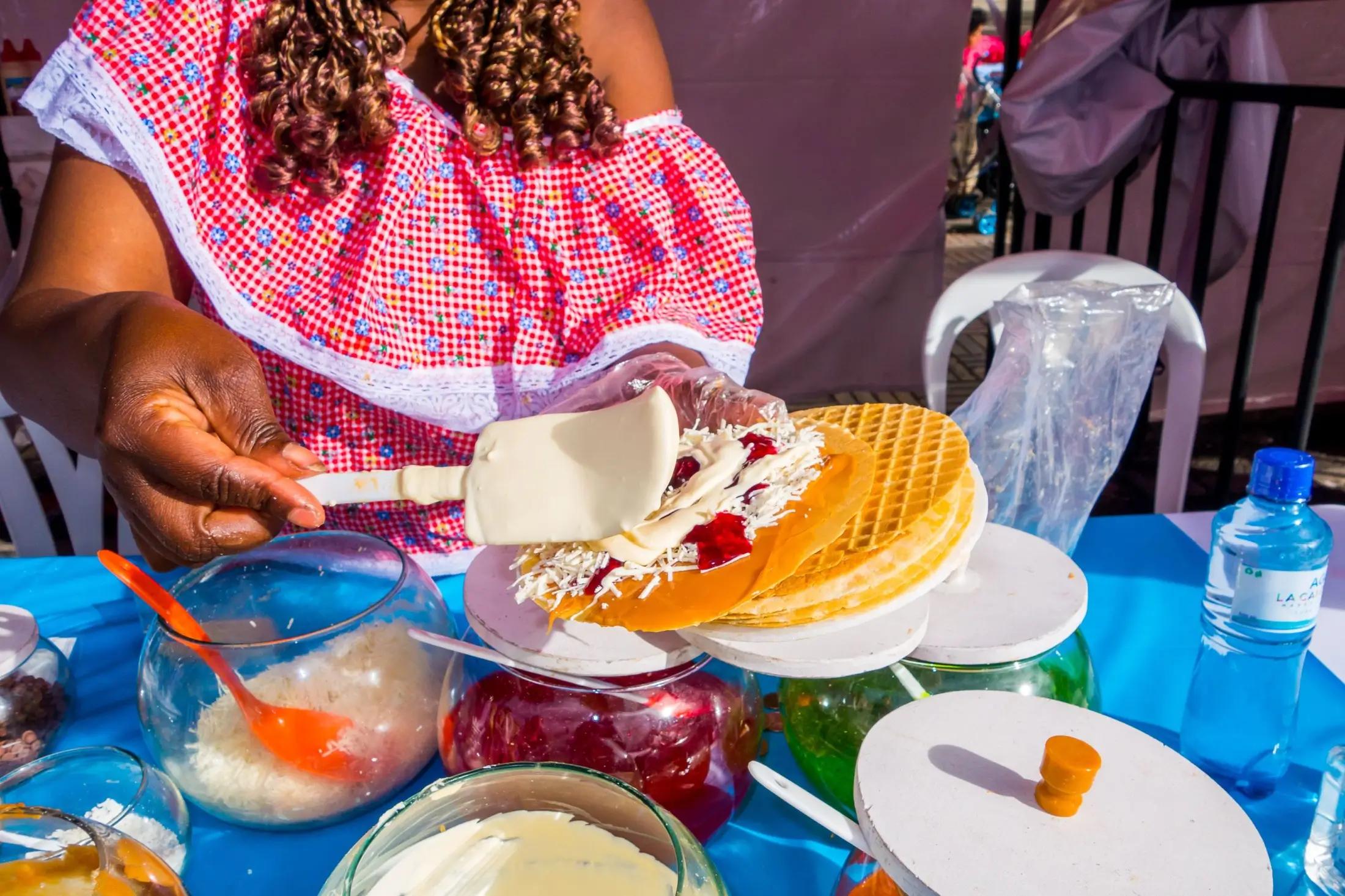 Žena tmavší pleti připravuje obleas ve stánku na ulici.