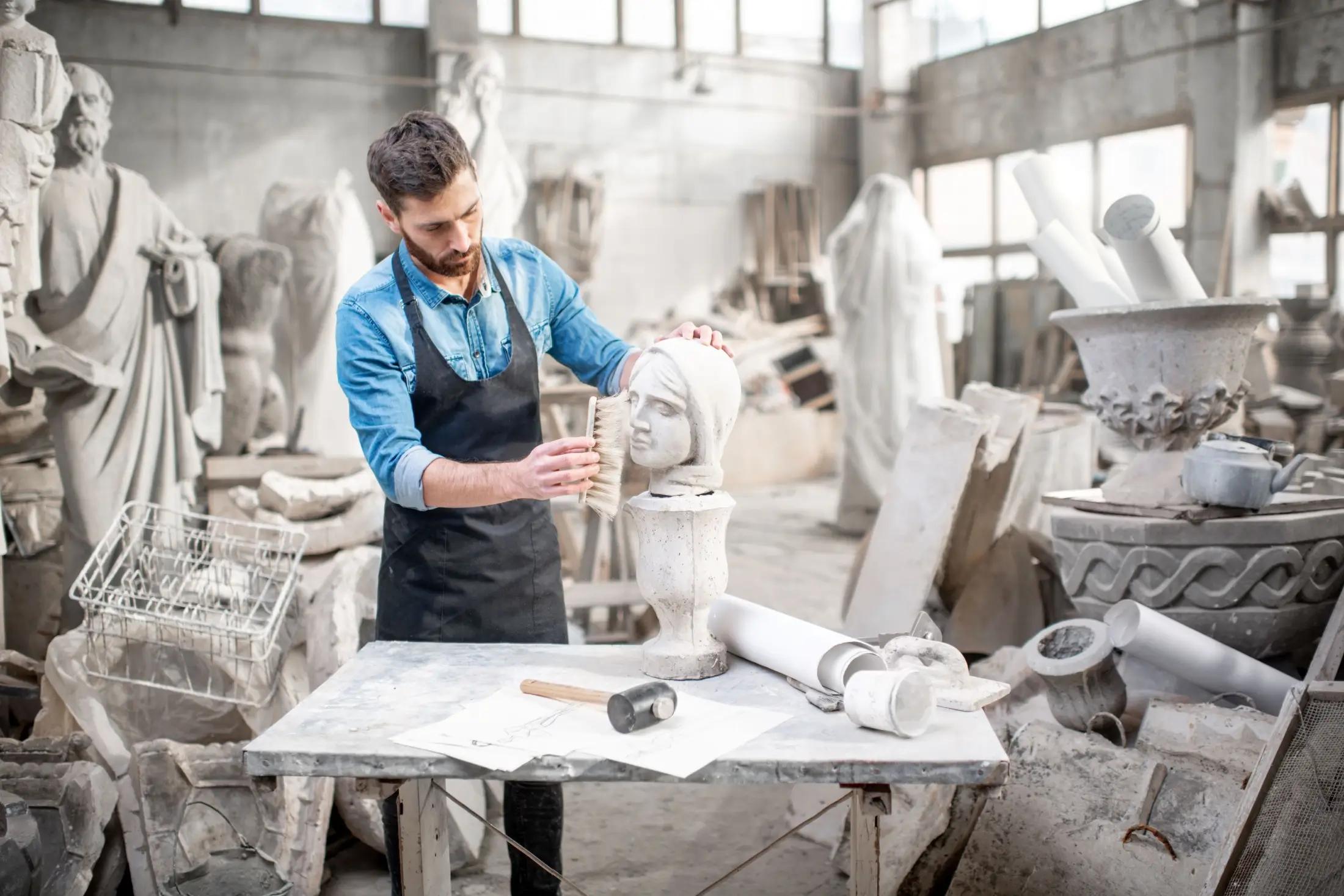 Mladý běloch stojí v jakési sochařské dílně. Před sebou má na stole postavenou hlavu sochy ženy, na které pracuje. V pozadí jde vidět několik dalších soch a nebo náčiní.