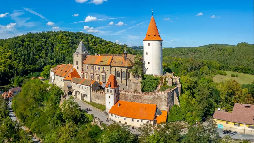 Letecký pohled na hrad Křivoklát a jeho okolí. Vidět jdou lesy v dáli a modrá obloha.