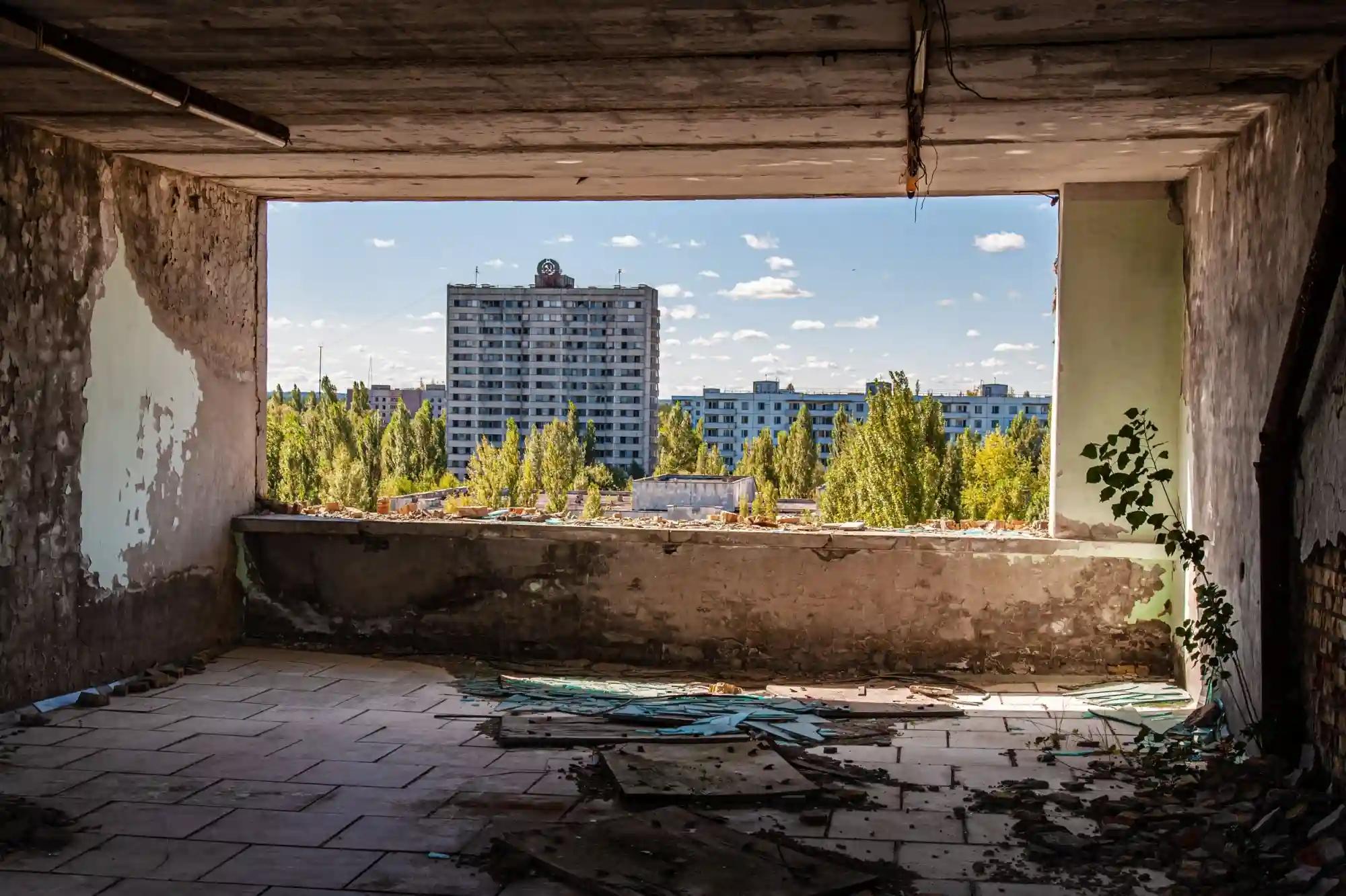 Pohled z rozpadlé budovy na prázdné zarostlé sídliště v Černobylu