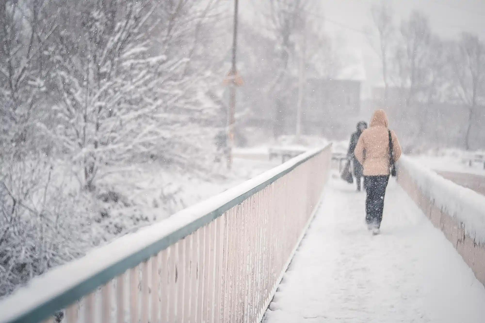 lidé jdou po zasněženém mostě ve městě