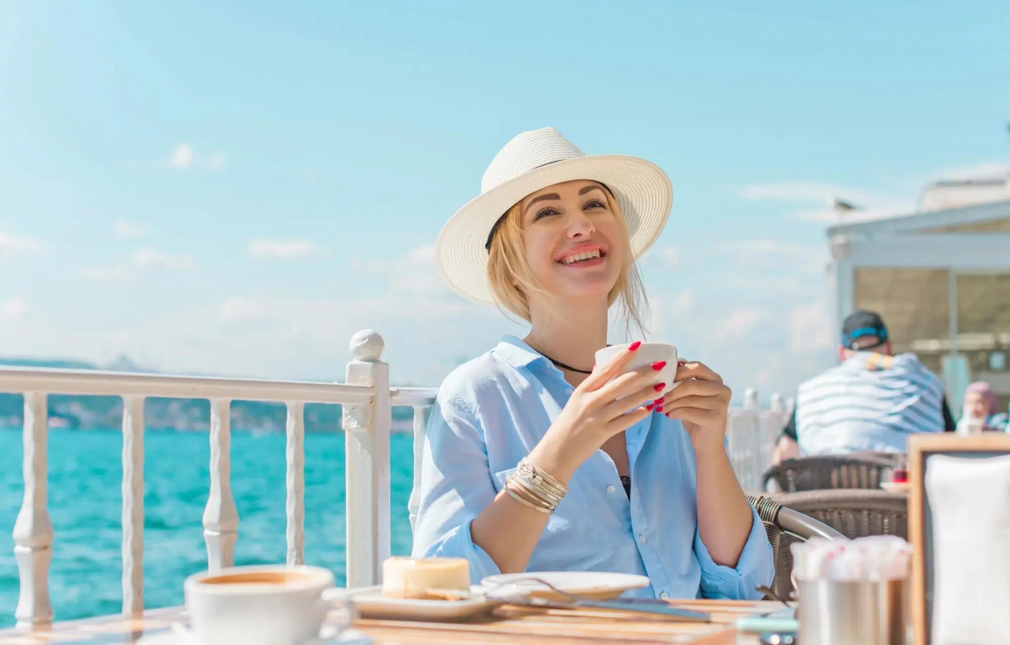 Blondýna si v kloboučku užívá snídani ráno u moře 
