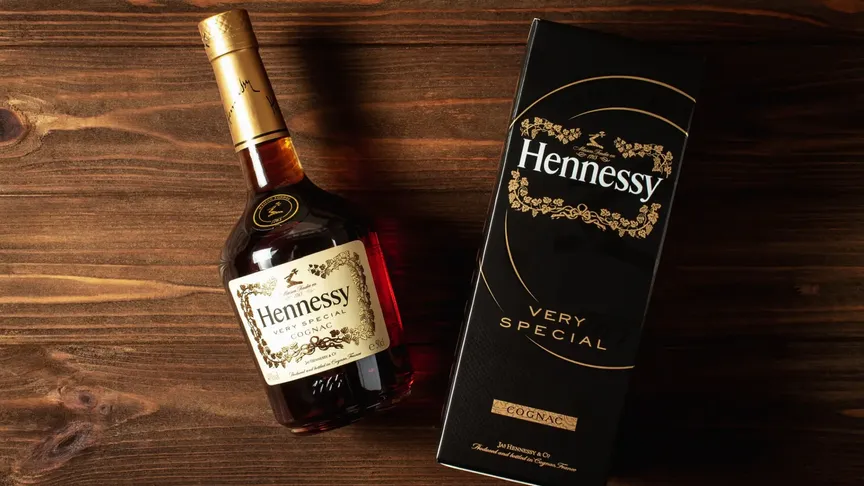 Na dřevěném stole leží láhev lihoviny Hennesy a její krabice.