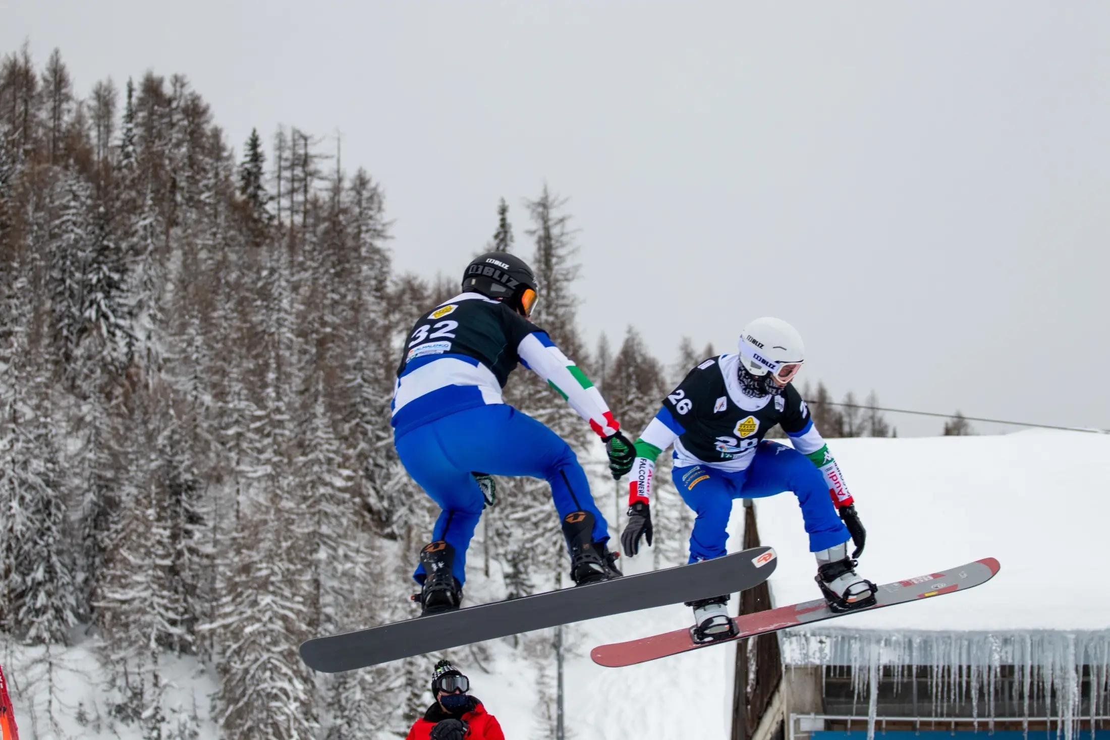 Škola v Chiesa Valmalenco. Instruktor učí žáka jezdít na snowboardu. Oba dva jsou ve skoku.