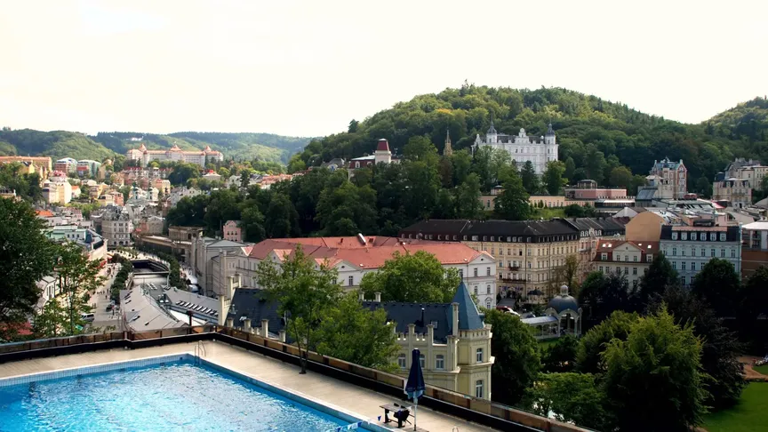 Panoramatický pohled na část střešního bazénu hotelu Thermal a okolí, které ze střechy je možné vidět. Vidět jsou unikátní budovy a zeleň stromů.