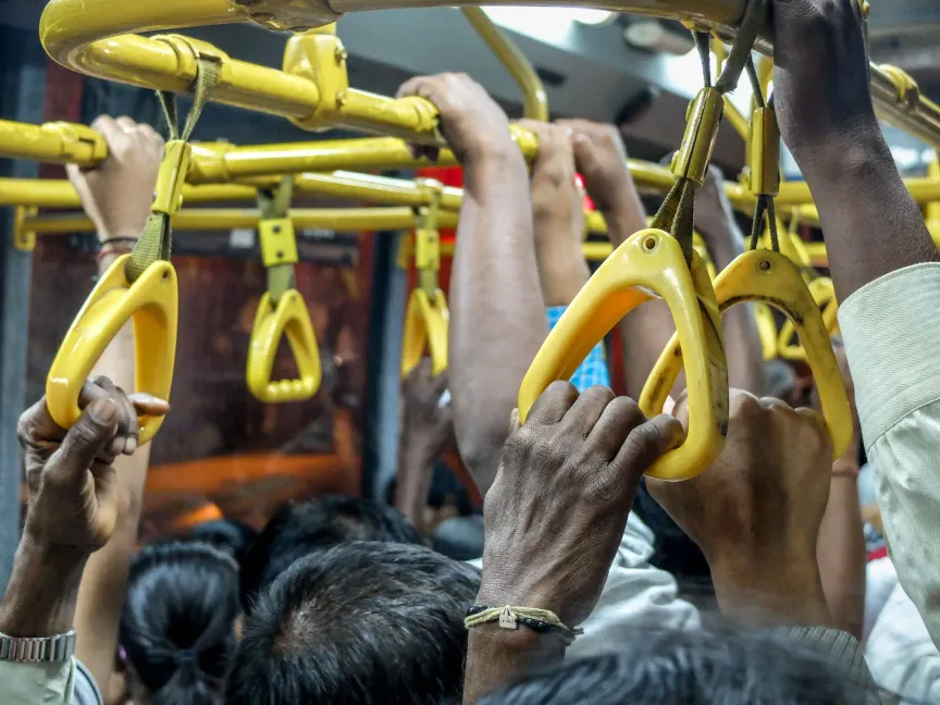 Na obrázku je přeplněný autobus, kde lidé musí stát a přidržovat se.