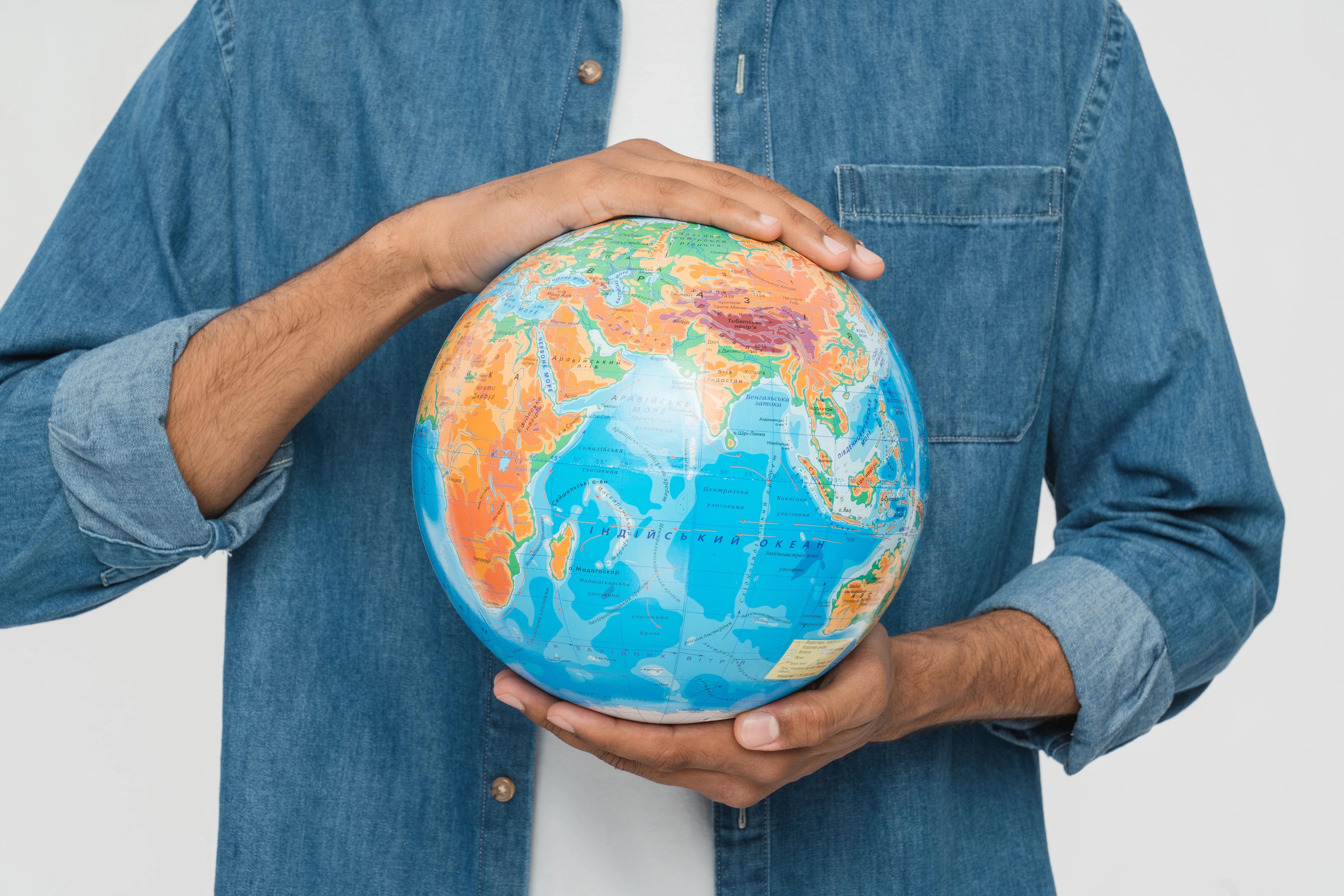 Zblízka oříznutý muž v džínové košili držící v dlaních globus Země 
