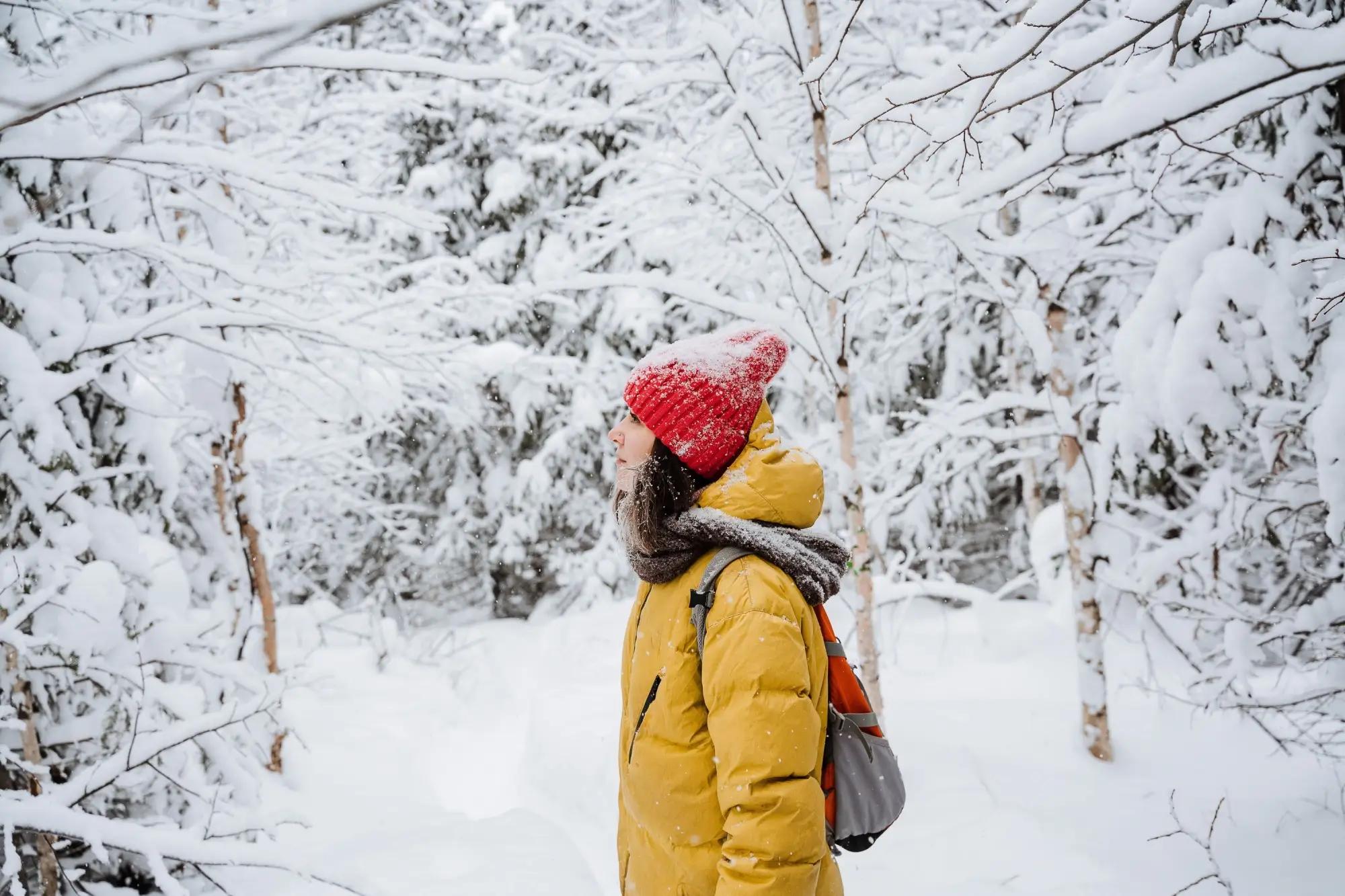 Žena stojí v bundě a čepici v zasněženém lese