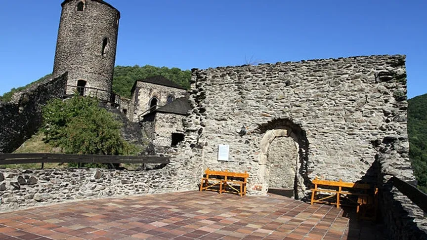 Pohled na kostkovanou růžovou dlažbu, vstupní bránu a věž