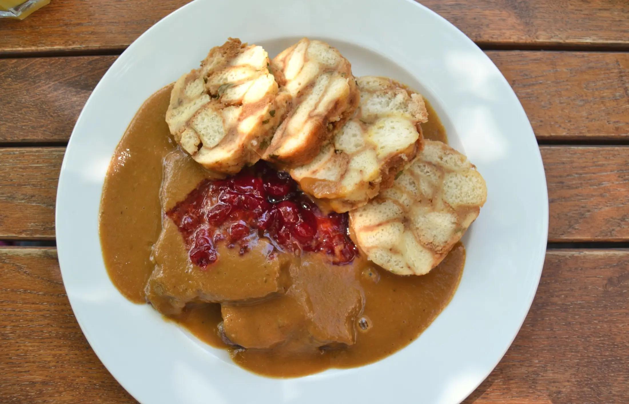 Svíčková se čtyřmi knedlíky, masem a brusinkami. Bílý talíř leží na hnědém stole.