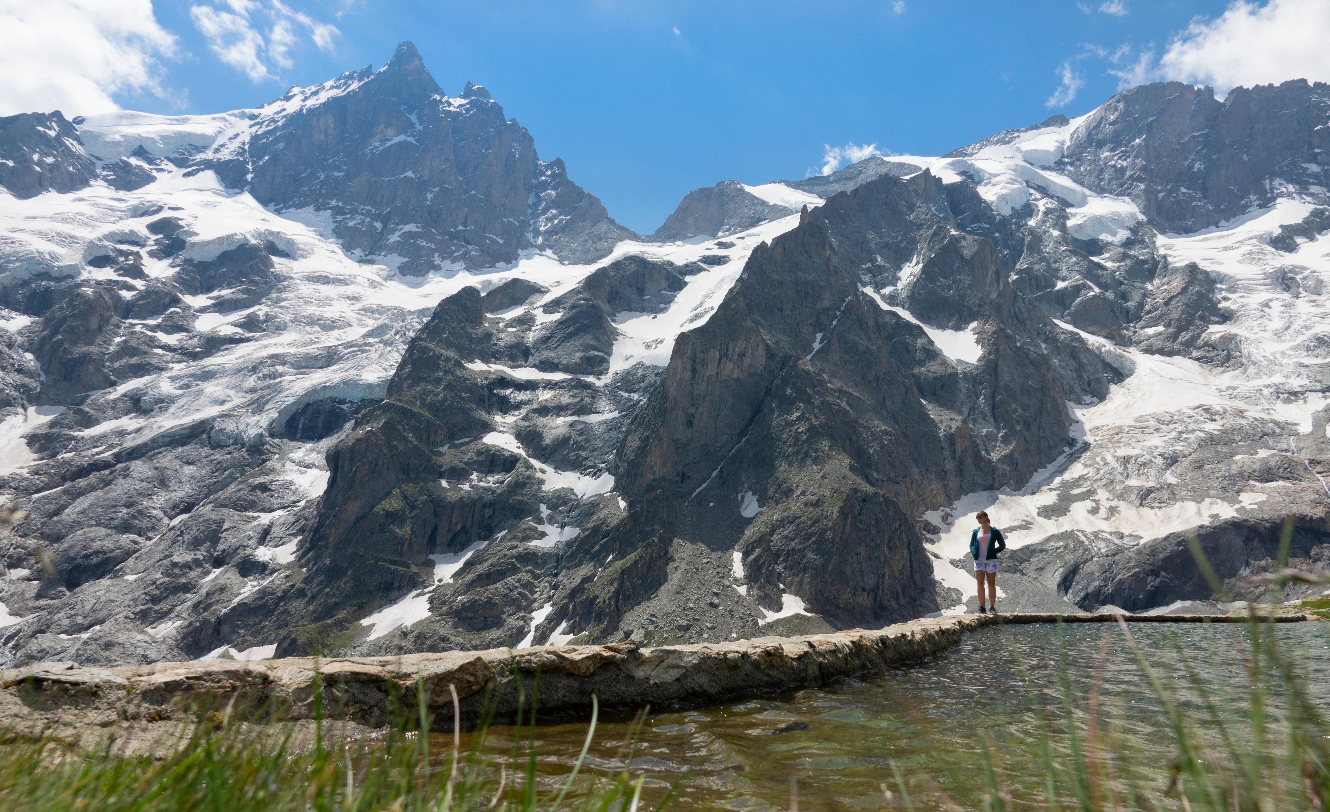 Letní pohled na ženu před horským střediskem La Grave, kde se částečně objevuje i sníh.