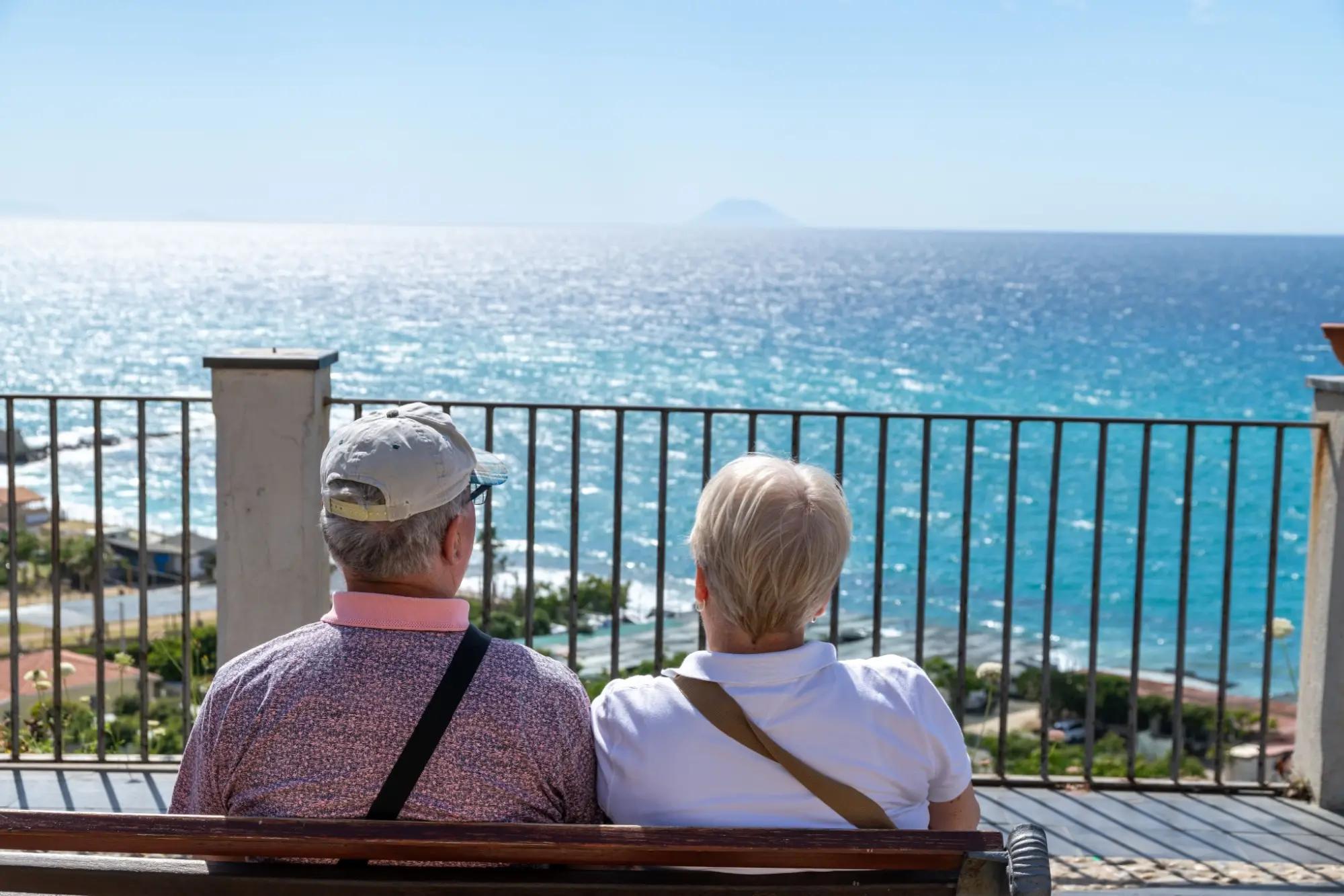 Dva senioři sedí na lavičce a dívají se na moře