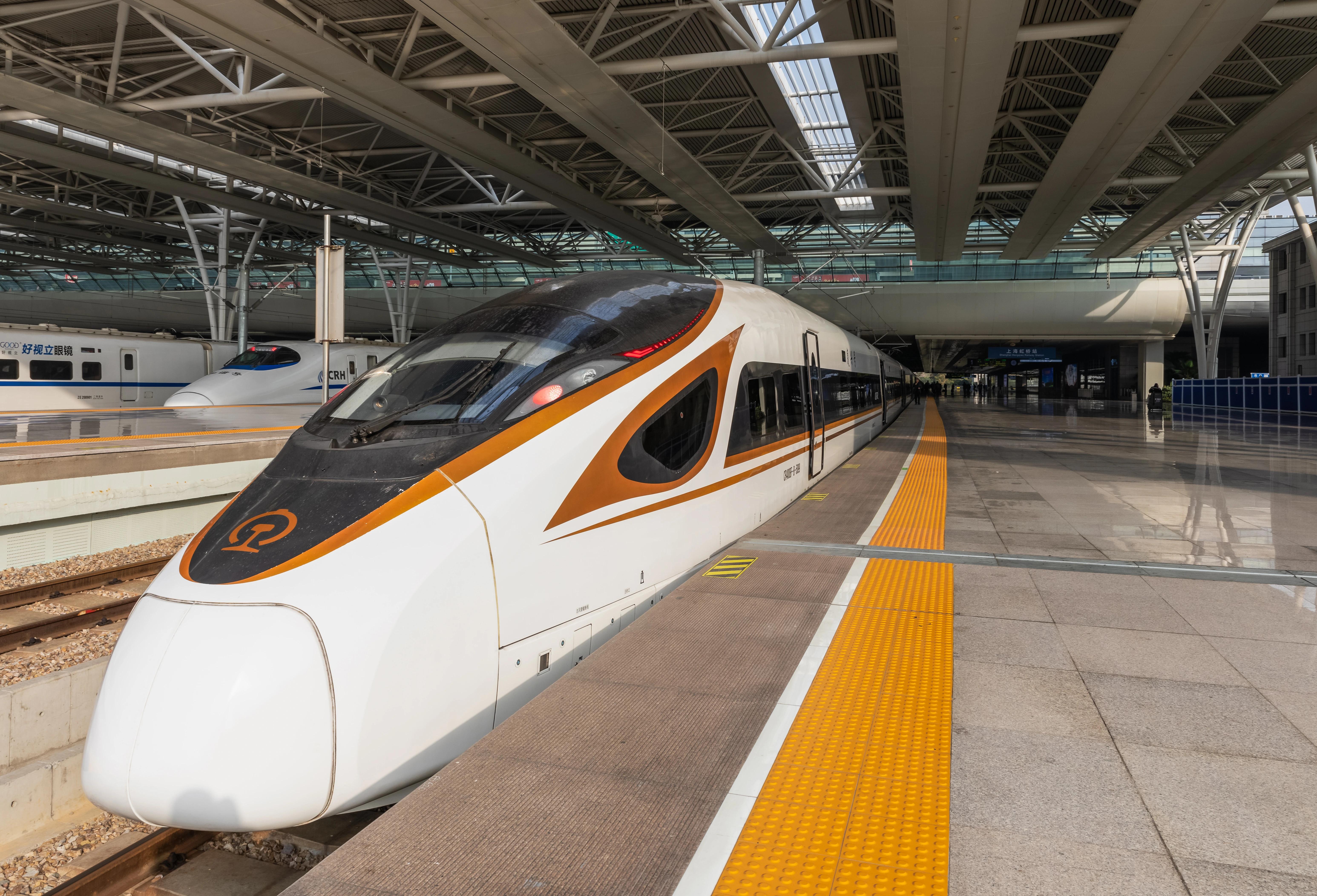 Vysokorychlostní oranžovo-bílý vlak Fuxing na nástupišti nádraží Hongqiao čeká na nástup cestujících, Šanghaj, Čína.