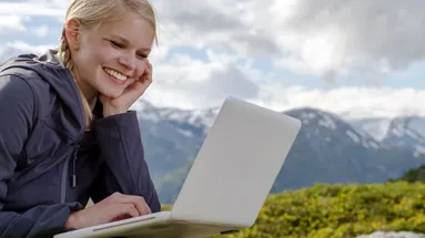 Žena je v horách a spokojeně se dívá do svého laptopu