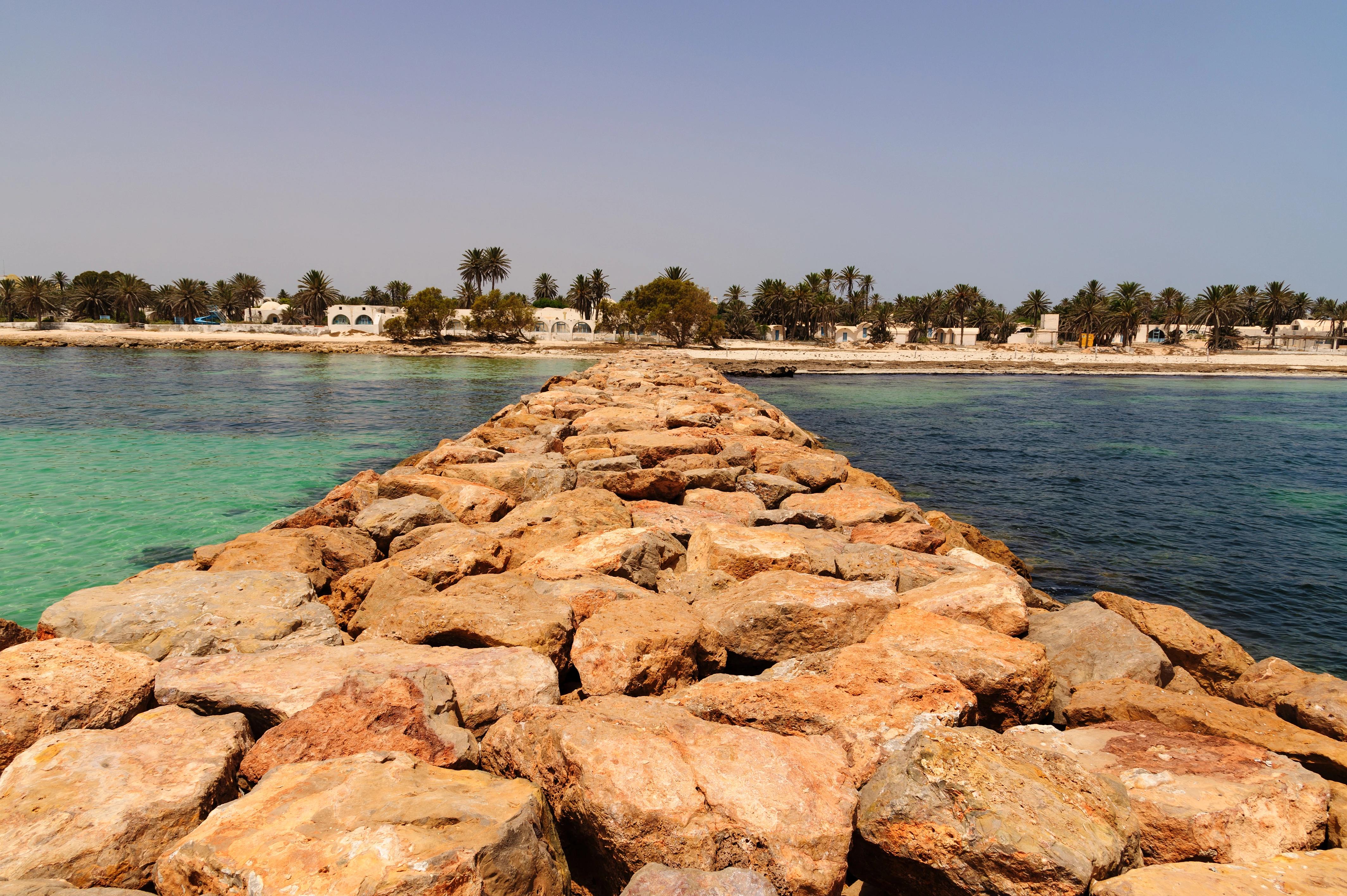 Kamenné molo vedoucí od osídlené pláže do moře, Djerba/Tunisko.