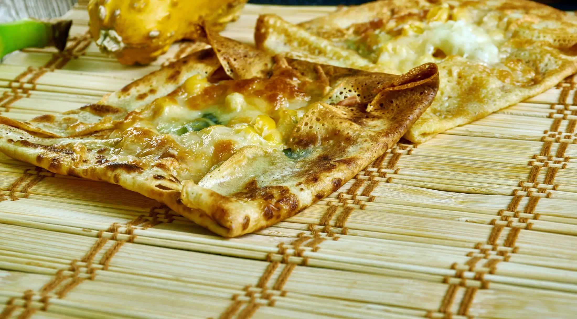 Dva tenké plátky zanzibarské pizzy. Ta má tvar čtverce a na povrchu sýr a zeleninu.