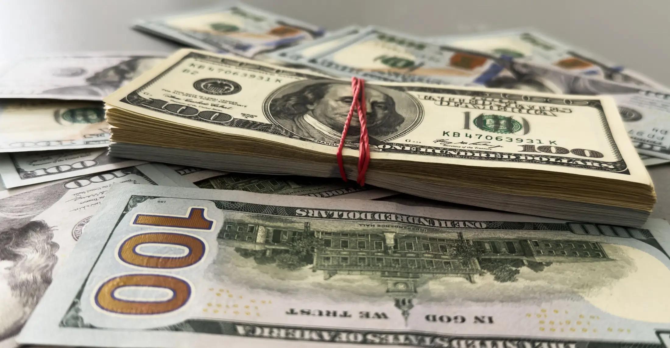 Stodolarové bankovky leží na šedém povrchu, nejspíše stole.