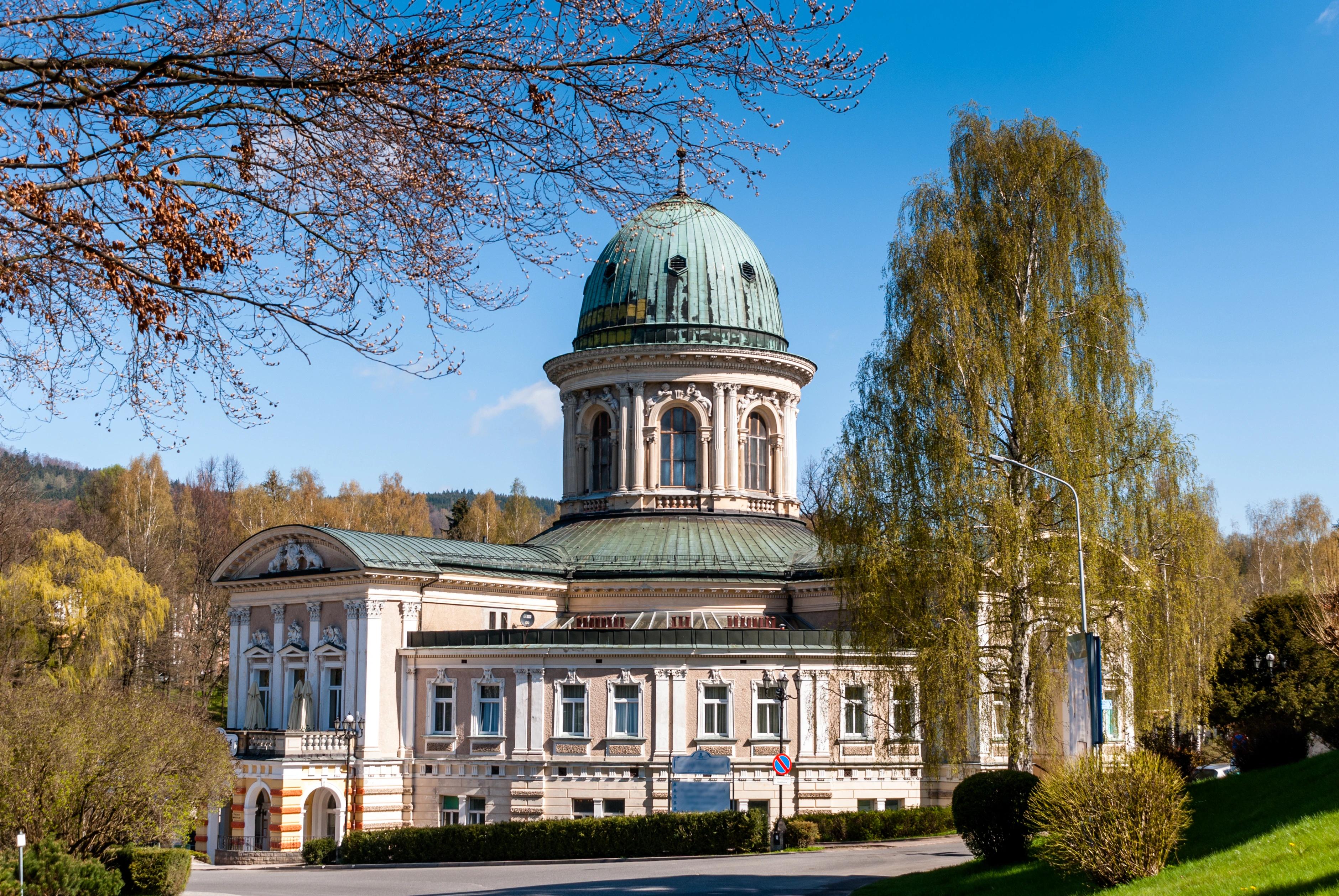 Budova lázní Ladek-Zdrój obklopena stromy za slunečného dne