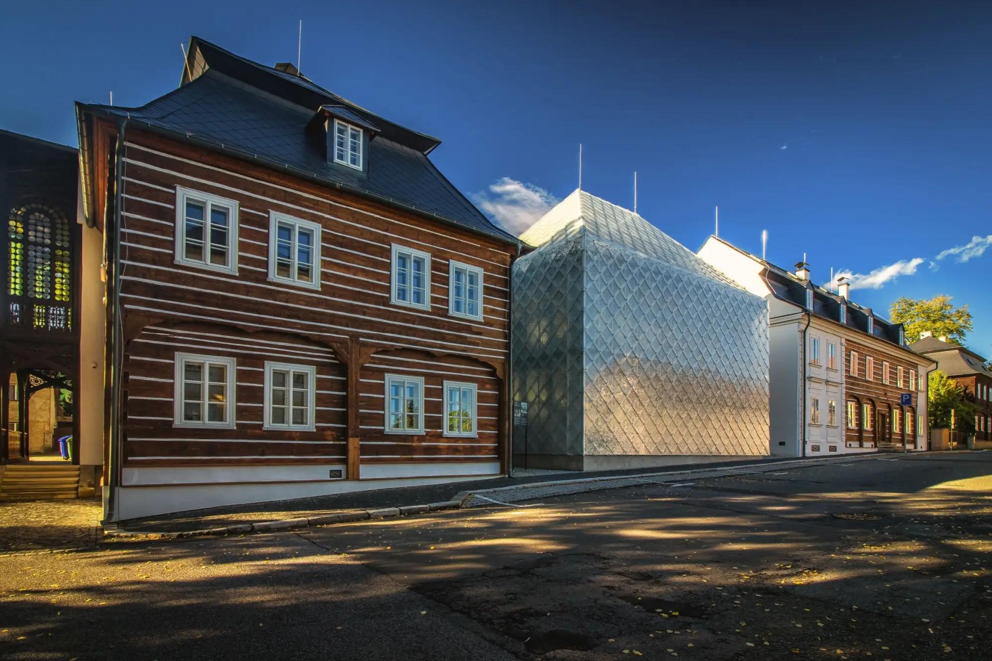 Skleněný dům stojící mezi roubenkami v Novém Boru