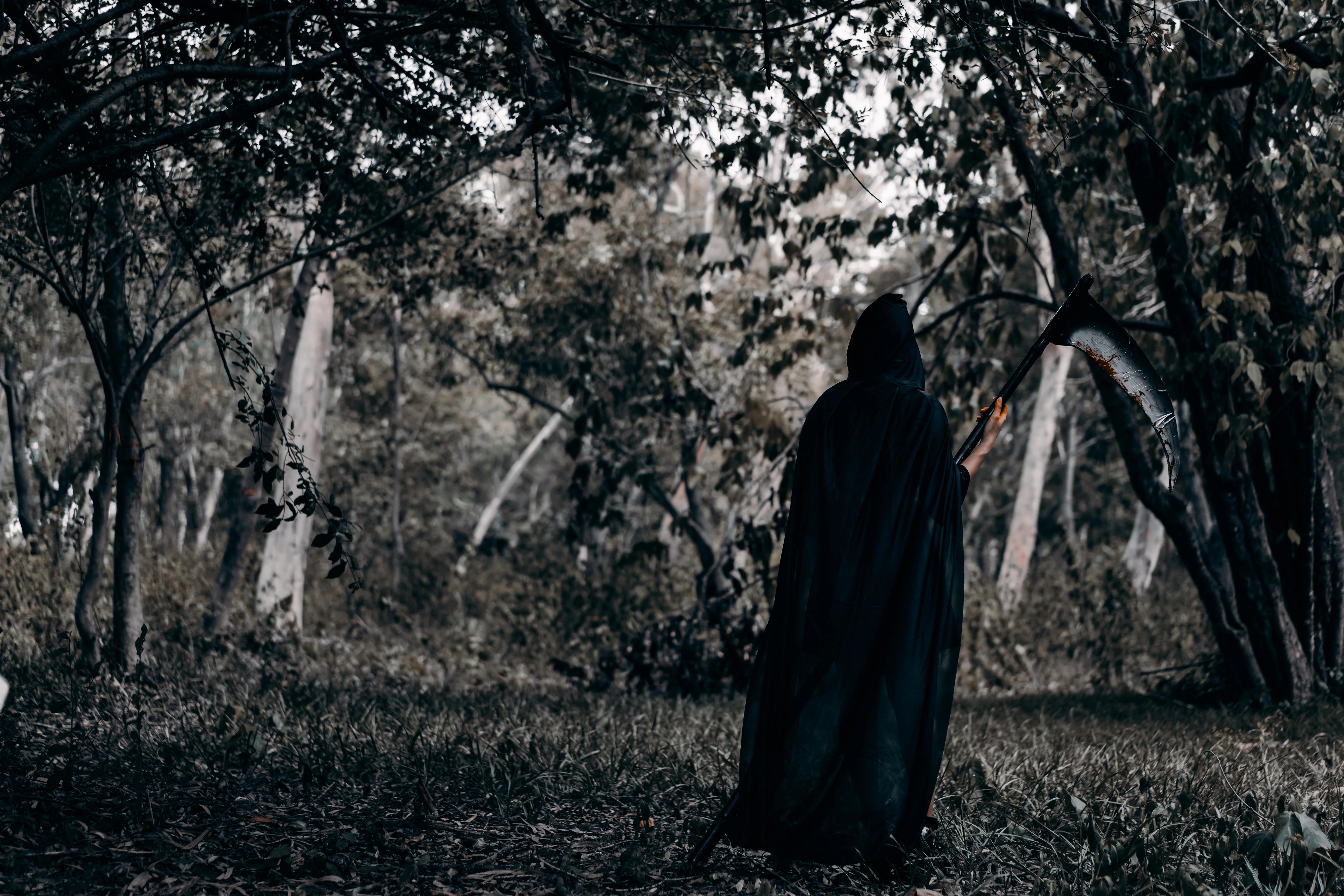 Podivná postava zahalena pláštěm uprostřed temného lesa.