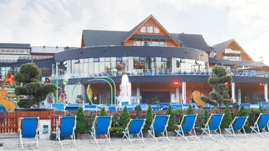 Obrázek ukazuje zevnějšek lázní, jde vidět hlavní budova a před ní písečná pláž a lehátka.