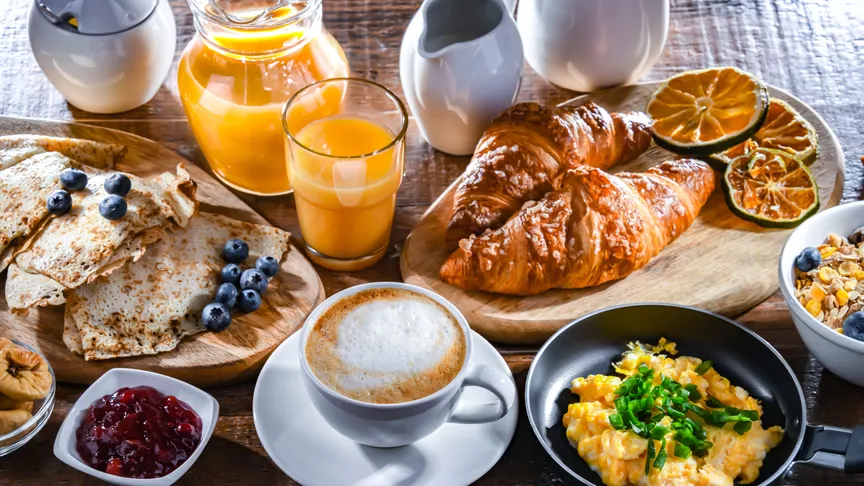 Bohatý snídaňový stůl s kávou, džusem, vajíčky, croissantem, palačinkami a dalších lahodných pokrmů.