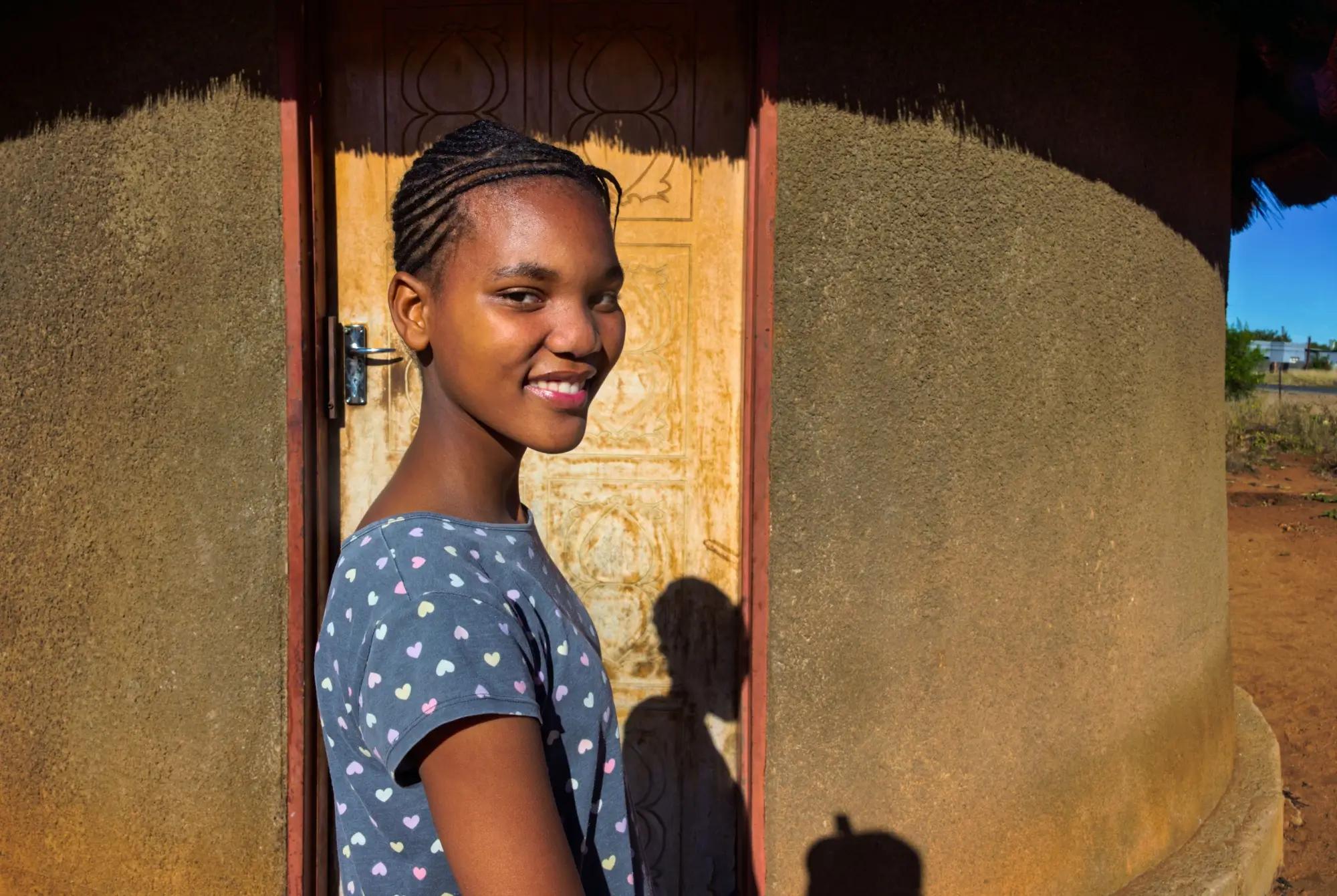 Zimbabwská dívka stojící před tradičním obydlím