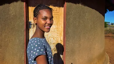 Zimbabwská dívka stojící před tradičním obydlím