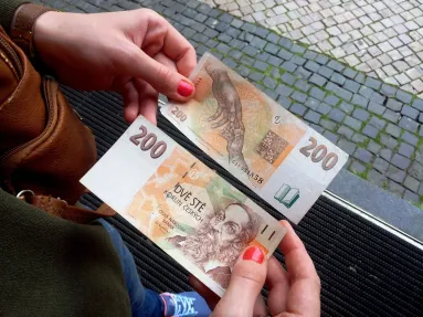 Ženské ruce drží dvě dvousetkorunové bankovky. Jednu z averzu a druhou z reverzu