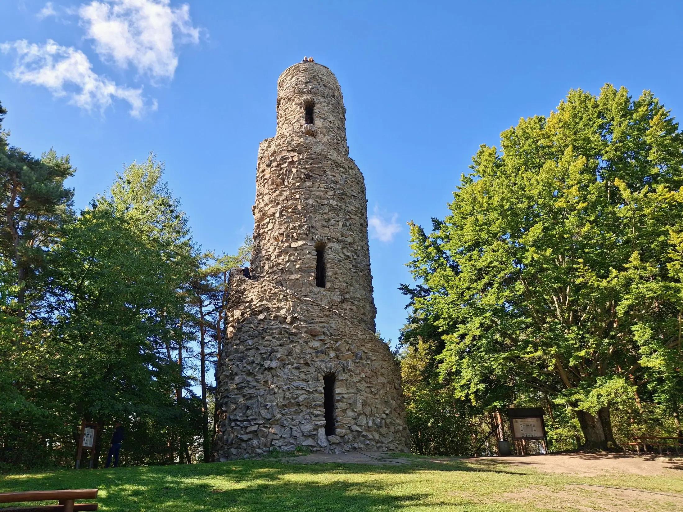 Kamenná rozhledna stojící na vrchu obklopená zelenými stromy
