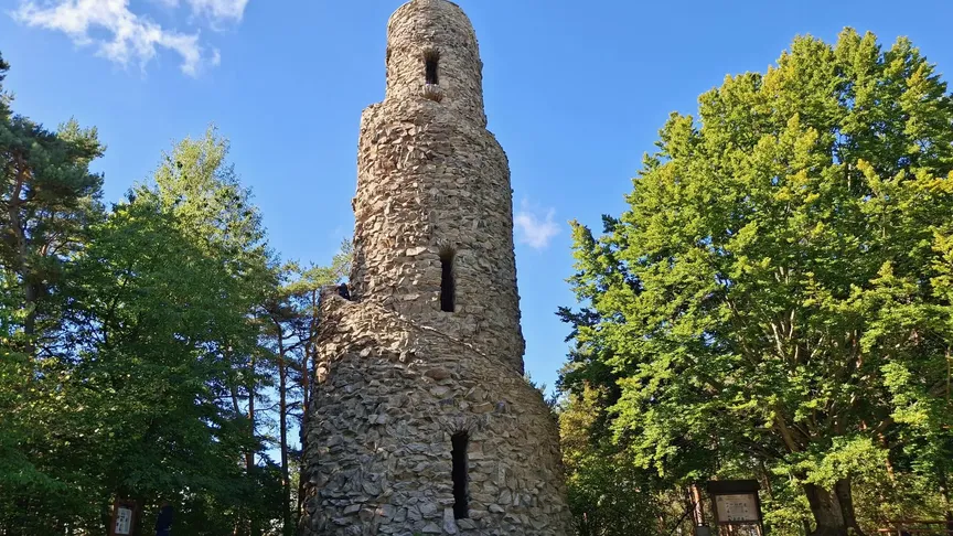 Kamenná rozhledna stojící na vrchu obklopená zelenými stromy