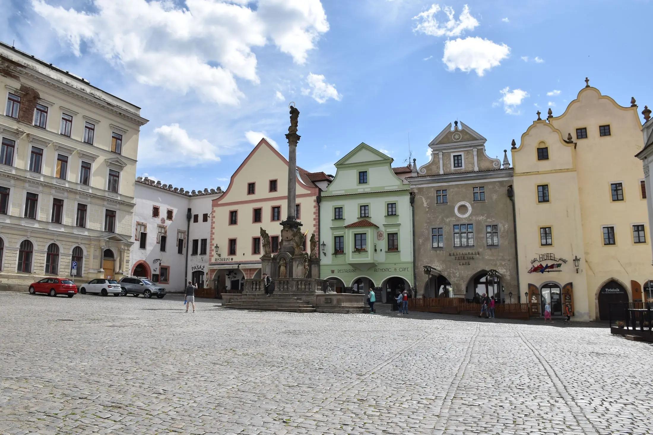 Náměstí Svornosti v Českém Krumlově za krásného slunného dne. Nachází se tu pár lidí.