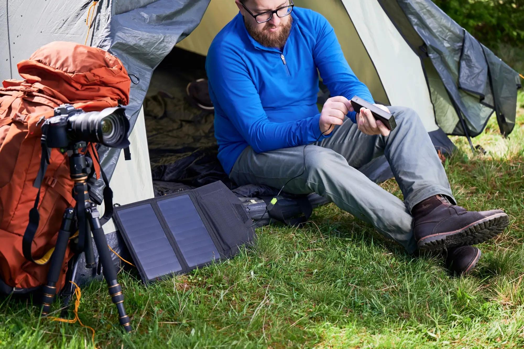 Kempující muž nabíjí svá zařízení pomocí solárních panelů