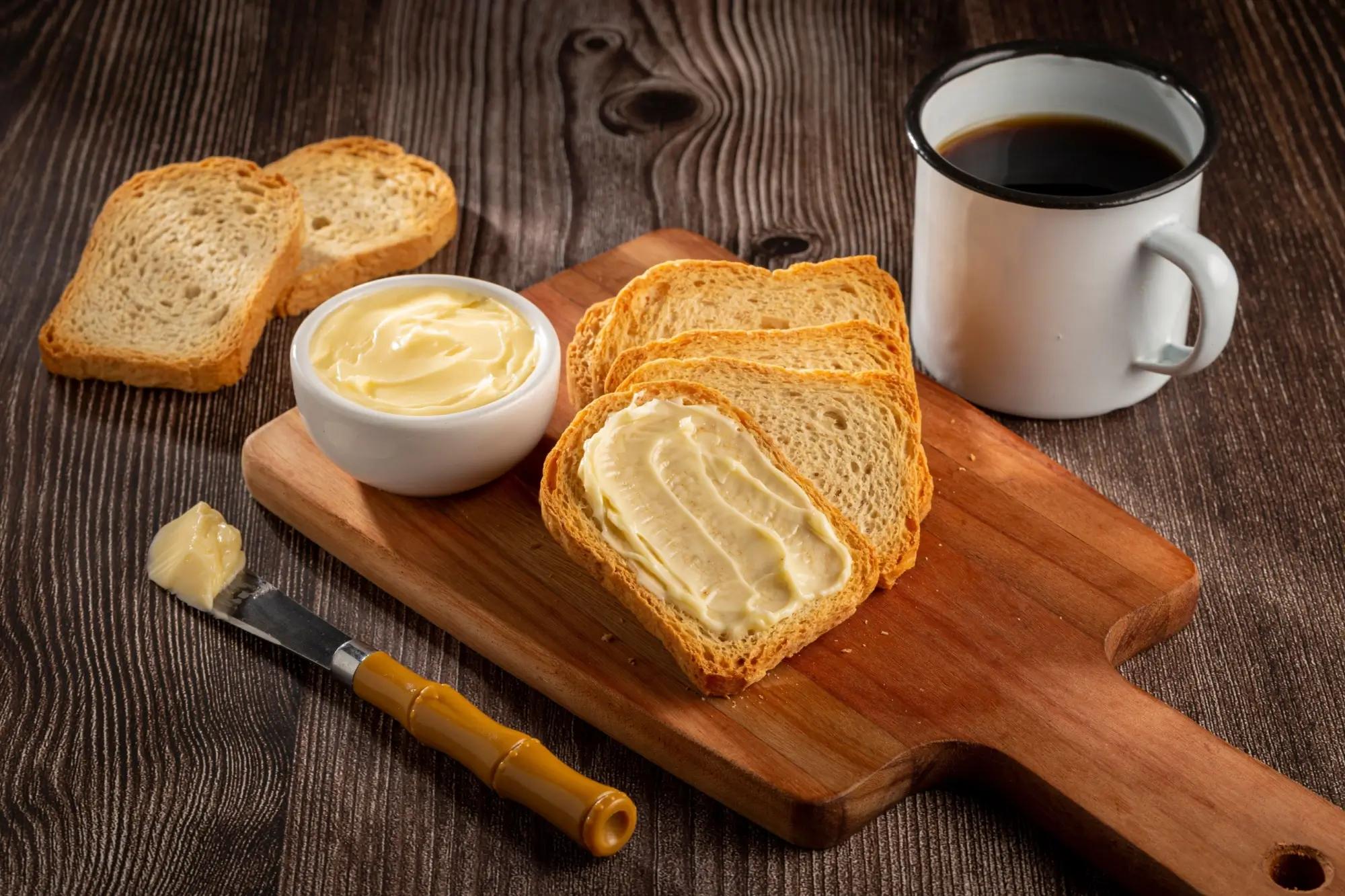 na prkénku položený máslo a chléb, vedle plecháček s kávou