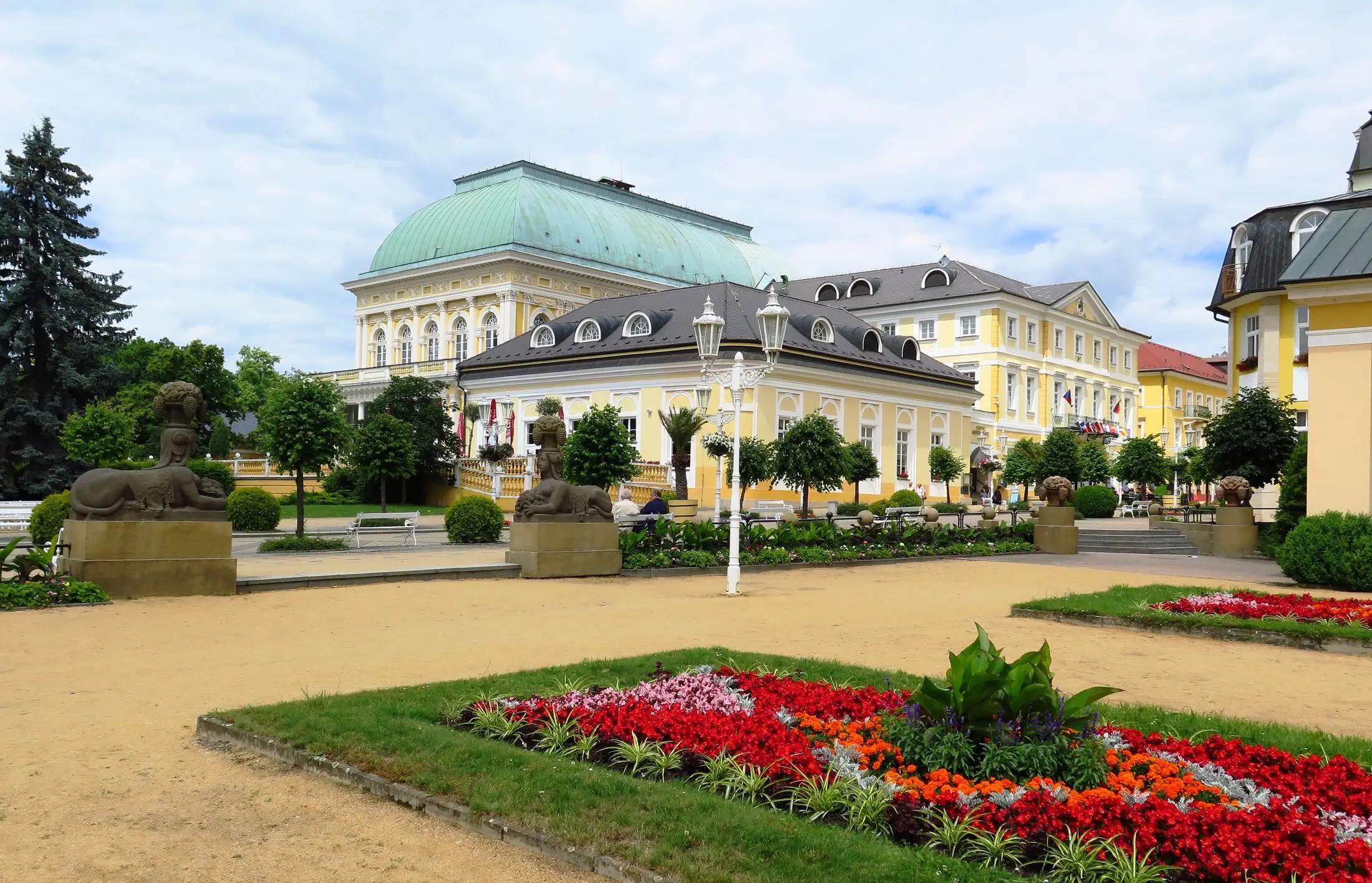 Okolí Františkových Lázní. Vidět jdou krásné lázeňské budovy a zahrady plné zeleně a květin.