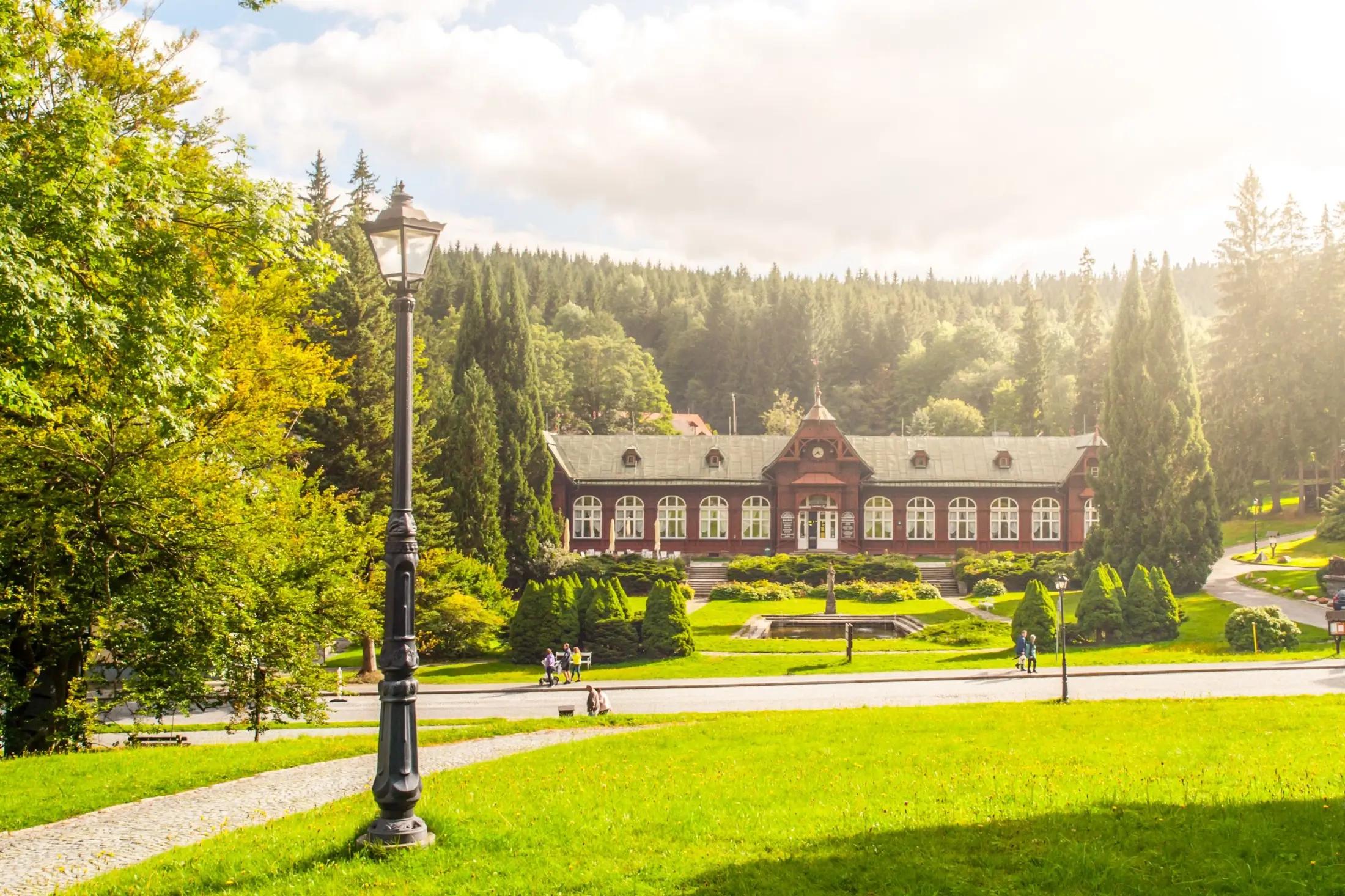 Budová lázní Karlova Studánka za krásný letní den. Okolí je plné zeleně.