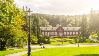 Budová lázní Karlova Studánka za krásný letní den. Okolí je plné zeleně.